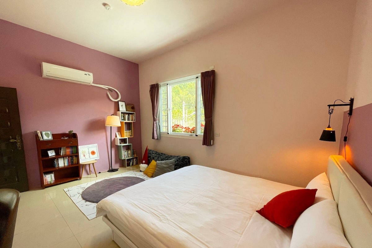 Een slaapkamer met een bed, een bureau, een boekenkast, een raam met gordijnen en een airconditioner.