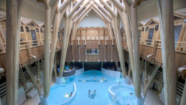 An indoor swimming pool with multiple lanes, surrounded by wooden structures and a central viewing area. - La Residence des Thermes (Bagnères-de-Bigorre)