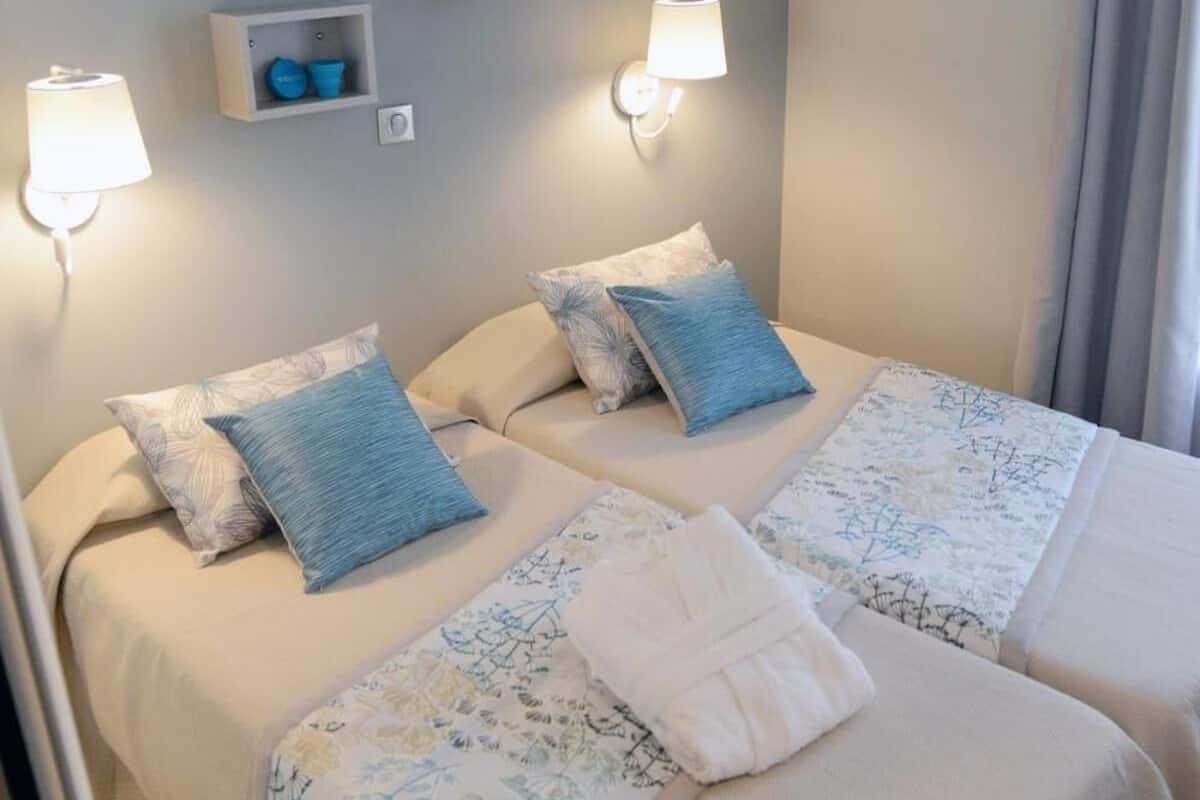 A double bed with floral bedding, two pillows, and a folded towel. There are two wall-mounted lights and a small shelf above the bed.