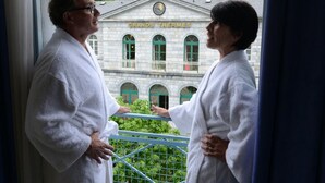 Two people in white bathrobes standing by a window overlooking a building labeled "GRANDS THERMES". - La Residence des Thermes (Bagnères-de-Bigorre)