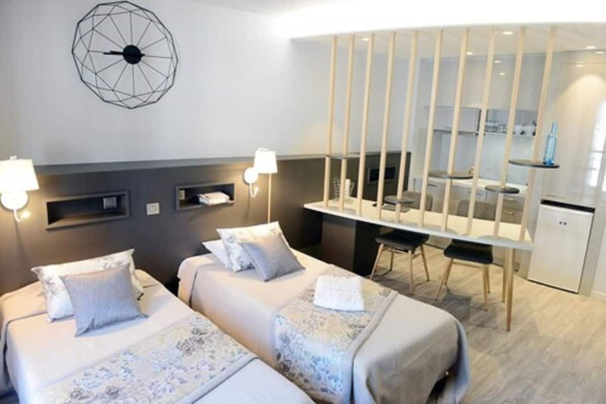 A hotel room with two beds, a desk, and a kitchenette.