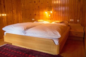 Une pièce aux murs lambrés, comprenant un lit, une table de chevet et un luminaire fixé au mur.