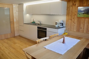 A modern kitchen with wooden cabinets, a built-in oven, a coffee maker, and a dining table with a vase of flowers. - Muxel Katharina - Apartment 2 - 5 people (Au)