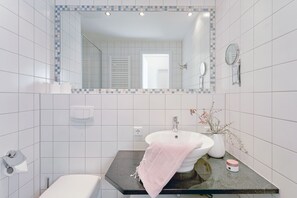 A bathroom with a white sink, a mirror with a blue-tiled frame, a towel, and a vase with dried branches. - Holiday Apartment Mercedes in Zinnowitz (Zinnowitz)