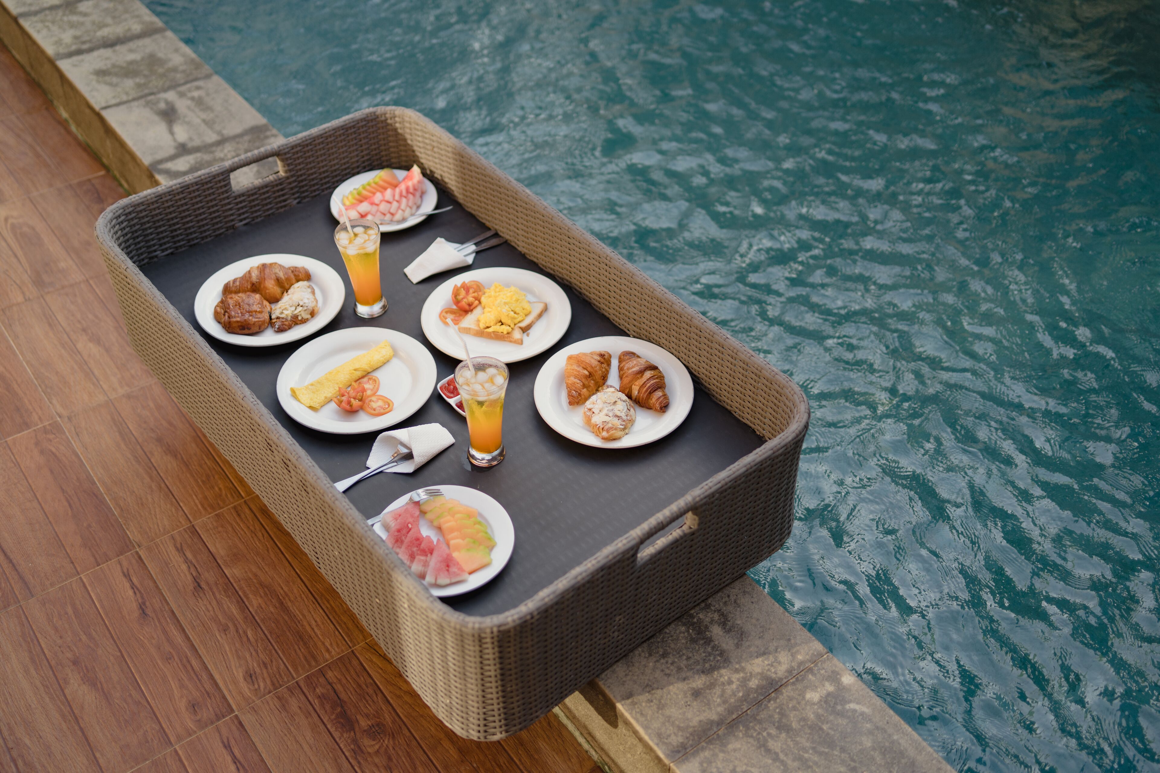 A wicker tray with breakfast items by a pool.