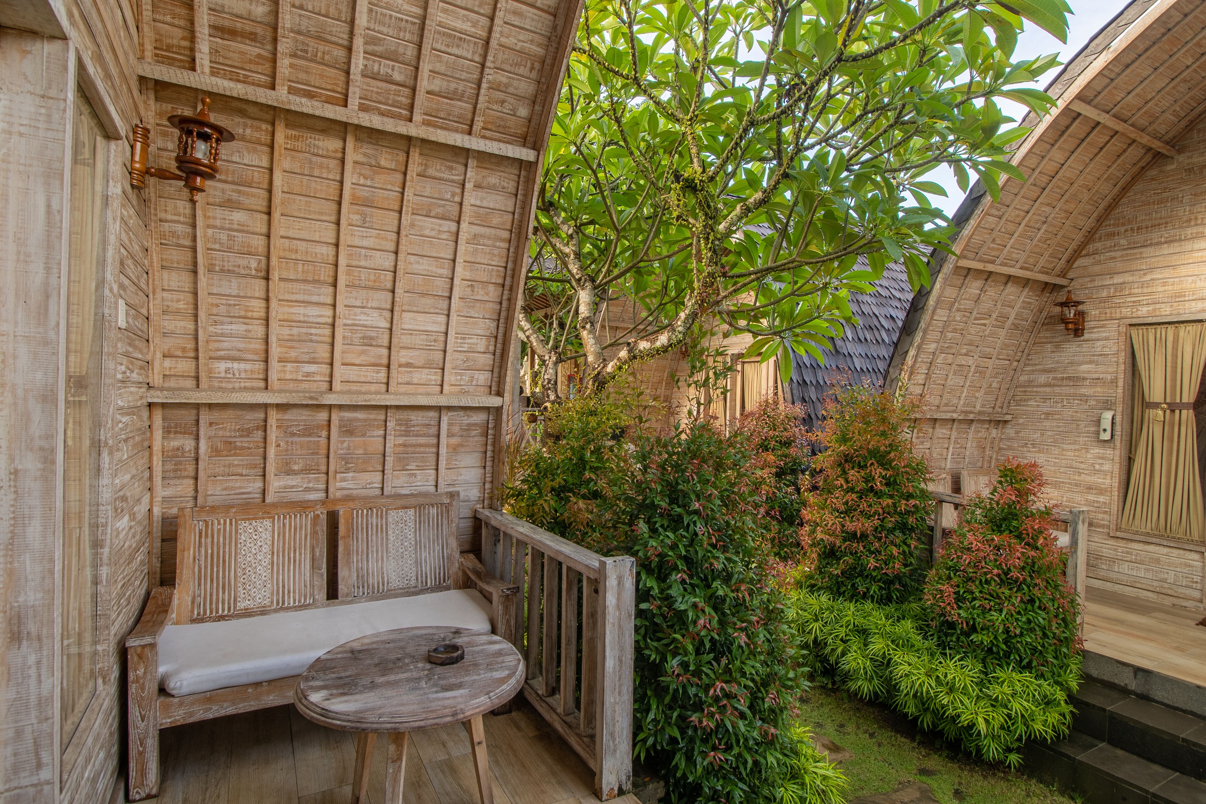 A wooden bench and table in a courtyard with a wooden wall and a tree.