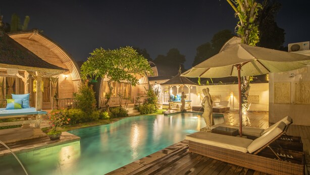 A nighttime pool area with lounge chairs, umbrellas, and a wooden deck. - Wana Shanti Villa (Mengwi)