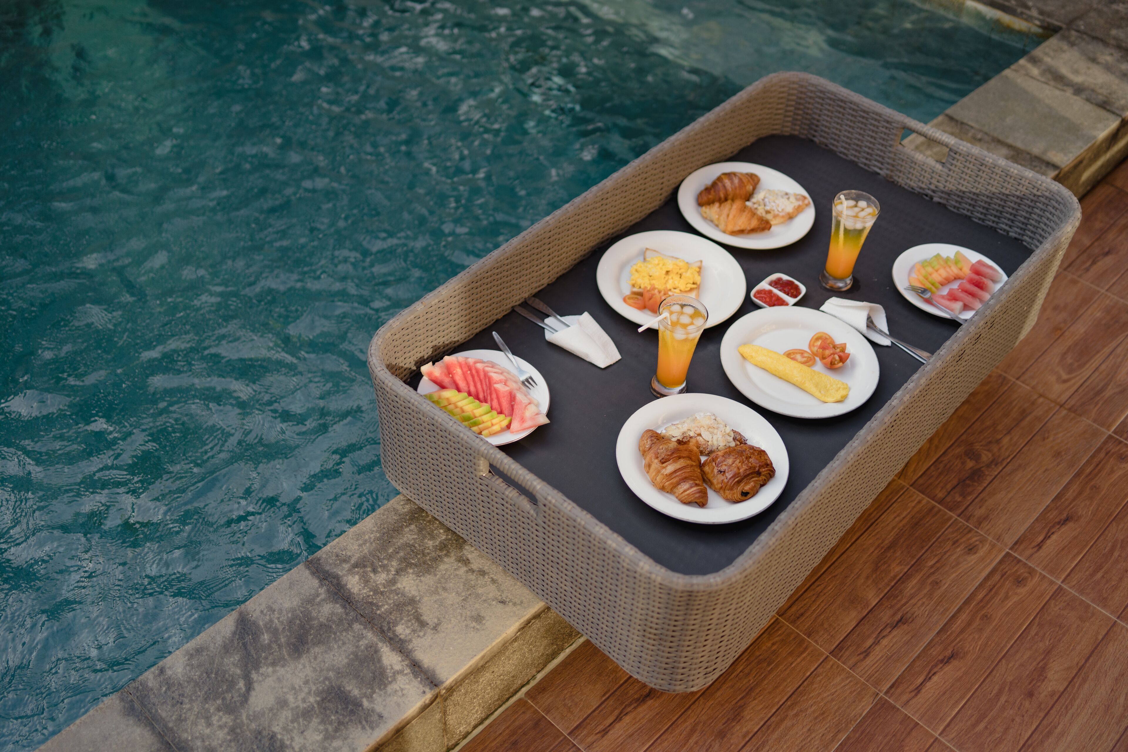 A wicker tray with breakfast items by a pool.