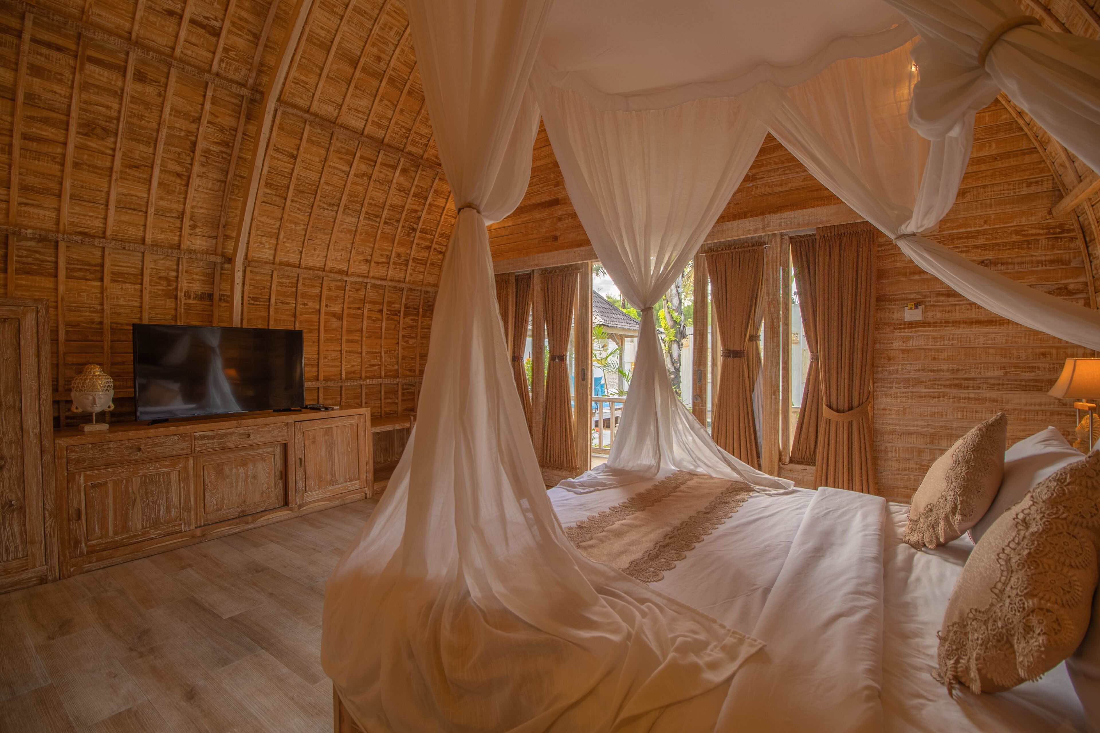 A room with a bed under a canopy, wooden walls, a television on a wooden cabinet, and windows with curtains.