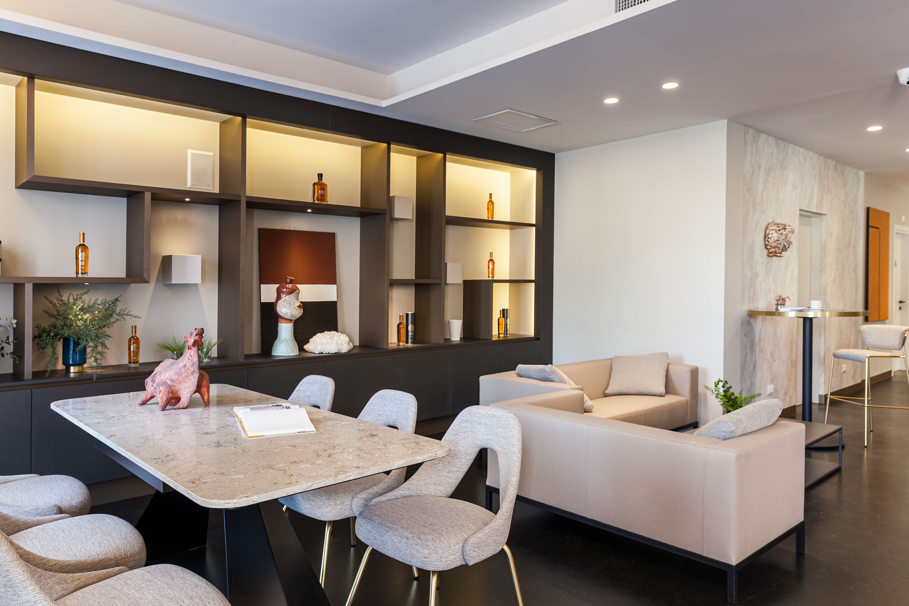 A modern living room with a large L-shaped sofa, a dining table with chairs, and built-in shelves with decorative items.