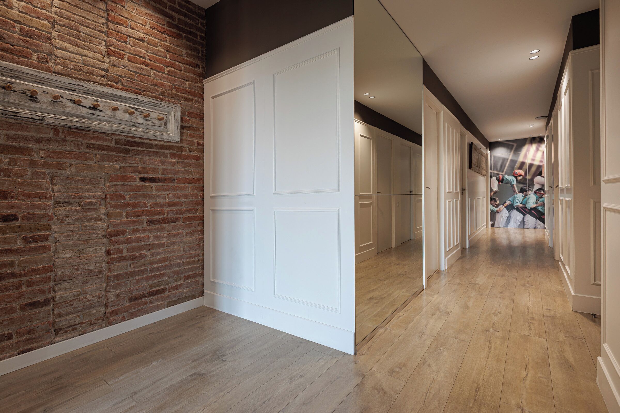 A hallway with a brick wall, white doors, and wooden flooring.