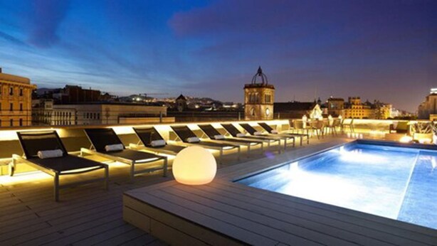A rooftop pool area with sun loungers and a large illuminated pool. - Enjoybcn Miro Apartments (Barcelona)