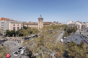A large building with a clock tower, surrounded by trees and a busy street with cars and buses. - Enjoybcn Miro Apartments (Barcelona)