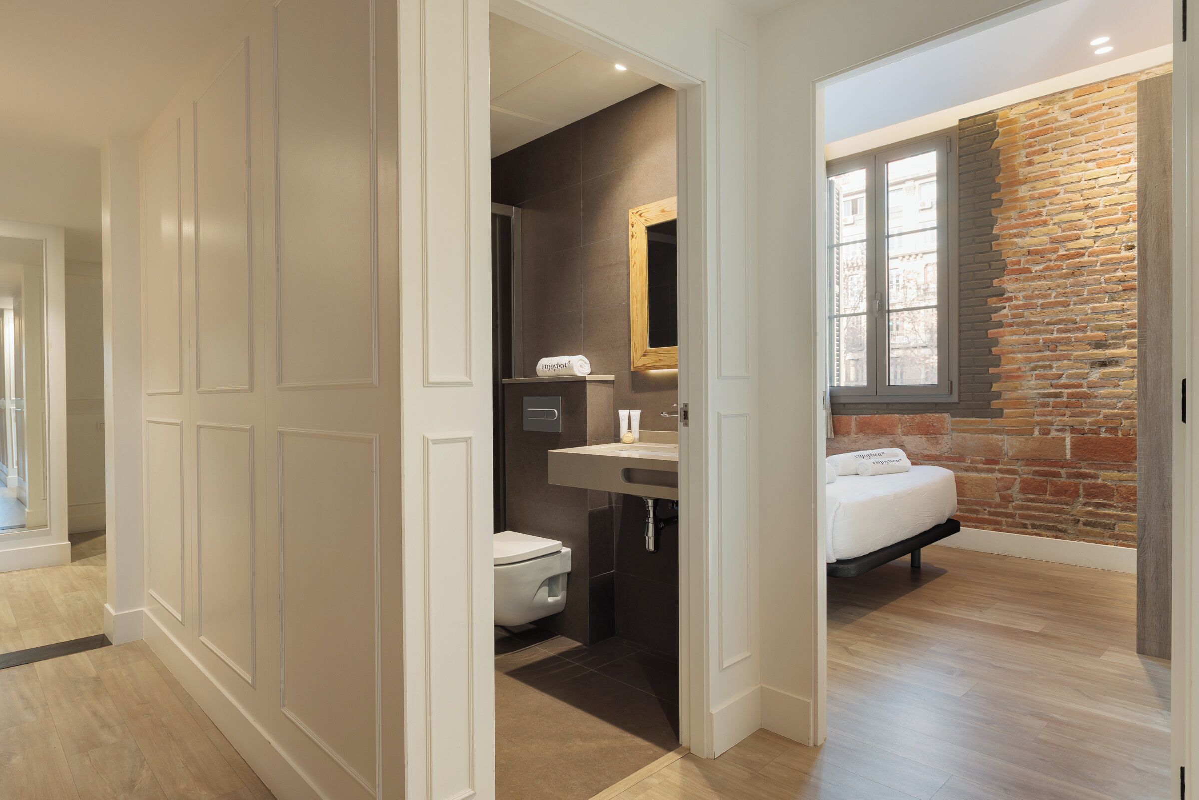 Une salle de bain moderne avec des toilettes, un lavabo et un lit, le tout agrémenté d’un mur en briques et d’une fenêtre.