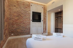 A hotel room with a brick wall, a white wardrobe, a wooden closet, and two towels with the text "enjoyben". - Enjoybcn Miro Apartments (Barcelona)