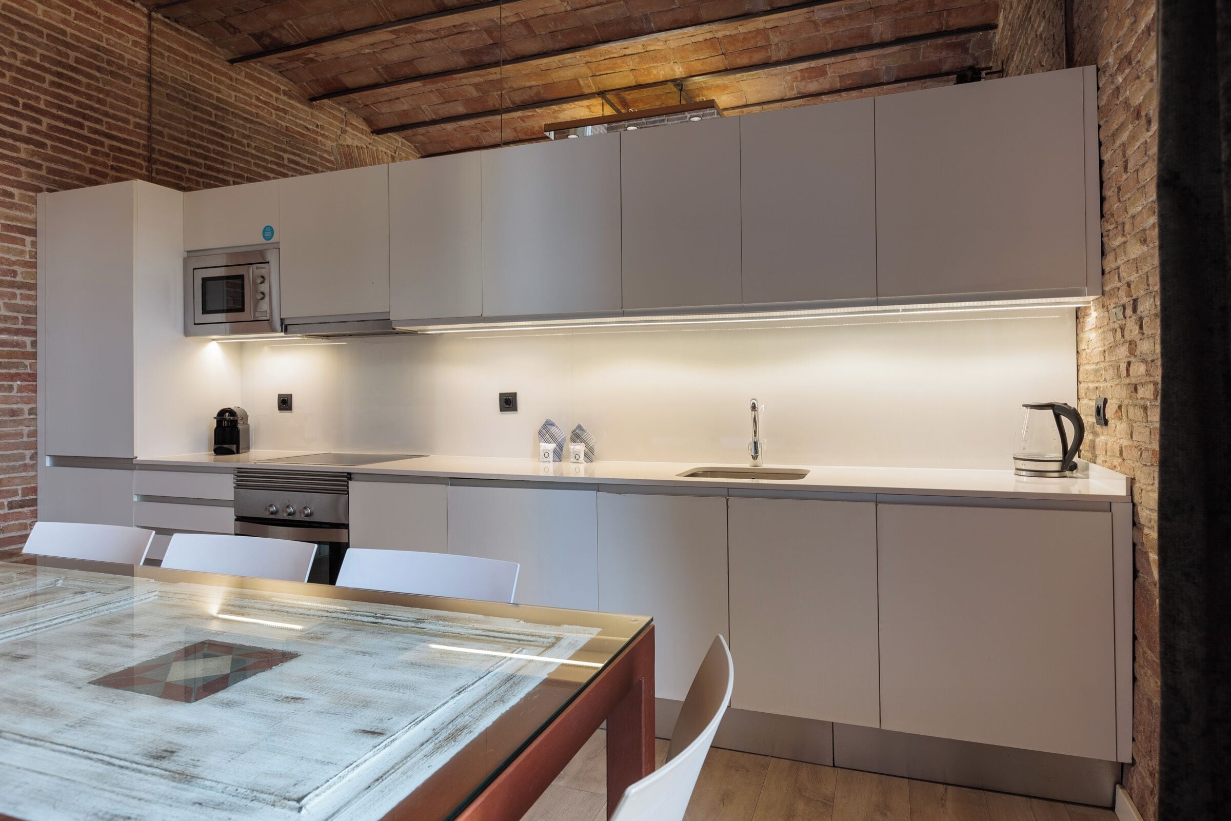 A modern kitchen with white cabinetry, a built-in microwave, and a stainless steel range hood.