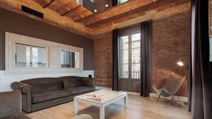 A modern living room with a brick wall, a large window, a sofa, a coffee table, and a chair. - Enjoybcn Miro Apartments (Barcelona)