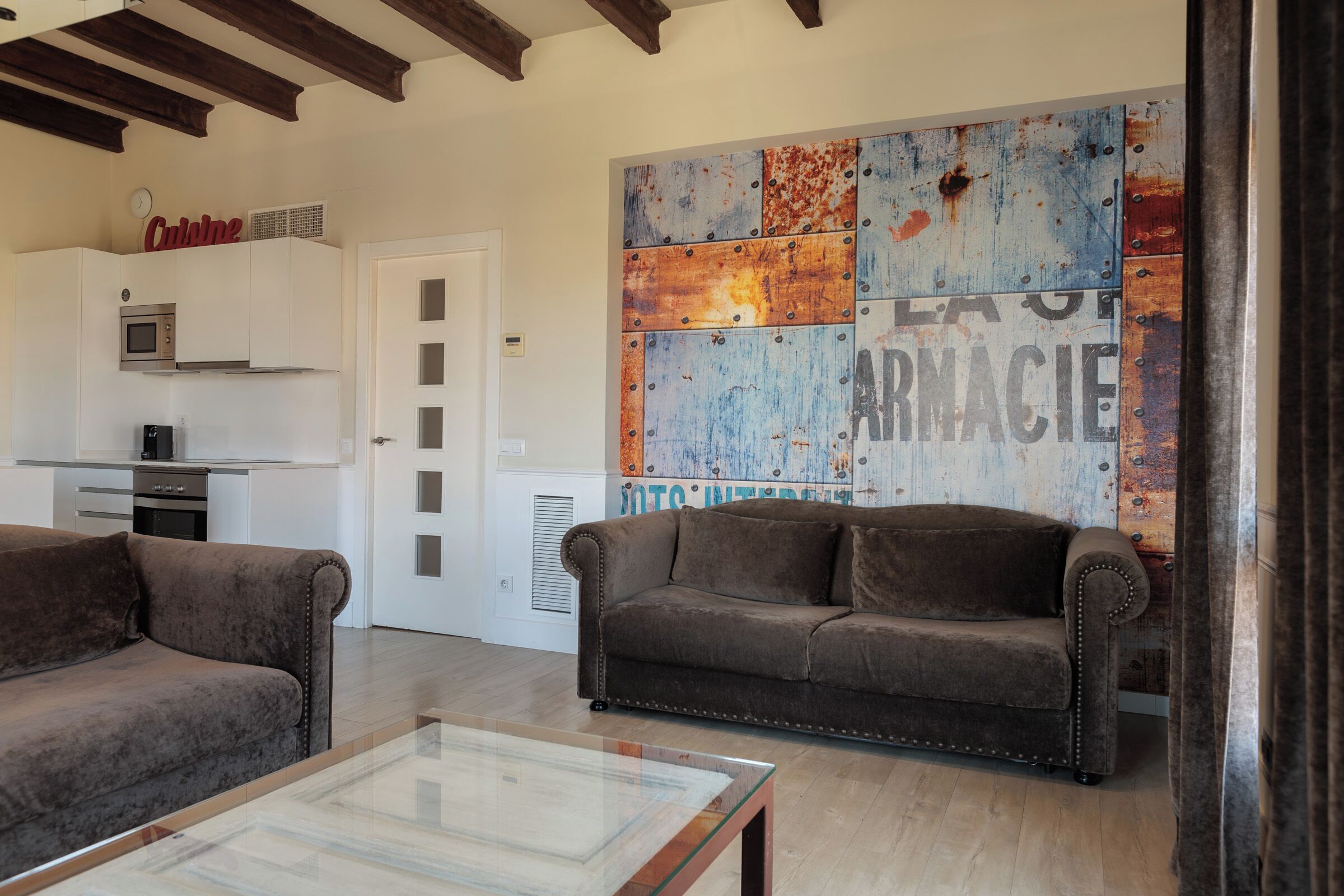 Una sala moderna con un sofá, una mesa de centro de vidrio y una zona de cocina con microondas y armarios.