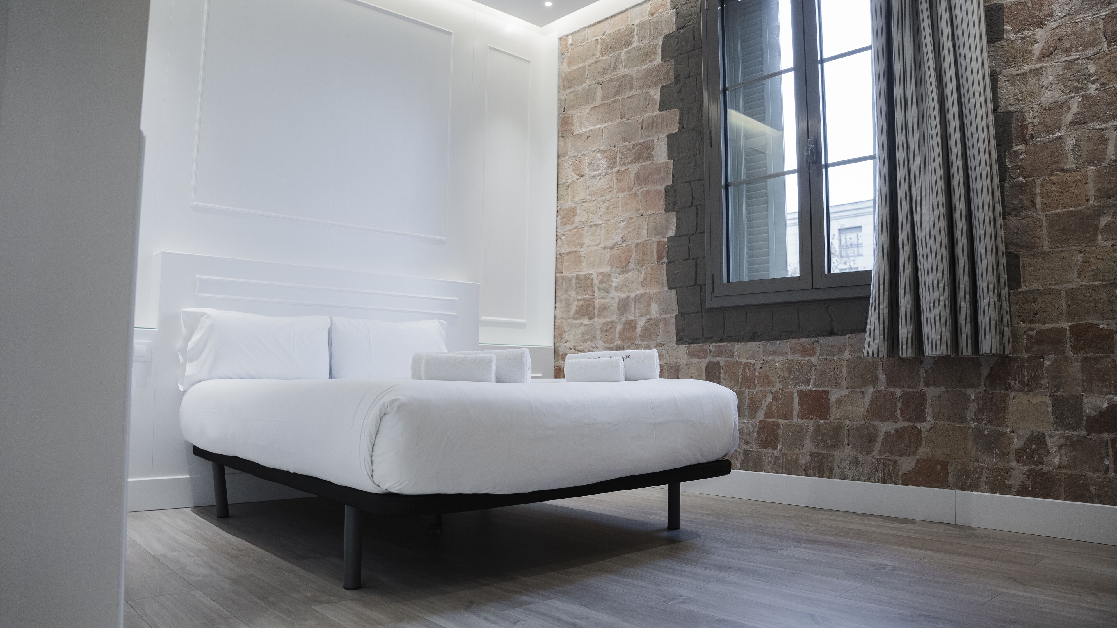 Un dormitorio moderno con cama, cabecera blanca y pared de ladrillo.