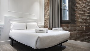 A modern bedroom with a large bed, white linens, and two towels with "enjoyben" branding. - Enjoybcn Miro Apartments (Barcelona)