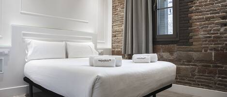 A modern bedroom with a large bed, white linens, and two towels with "enjoyben" branding.
