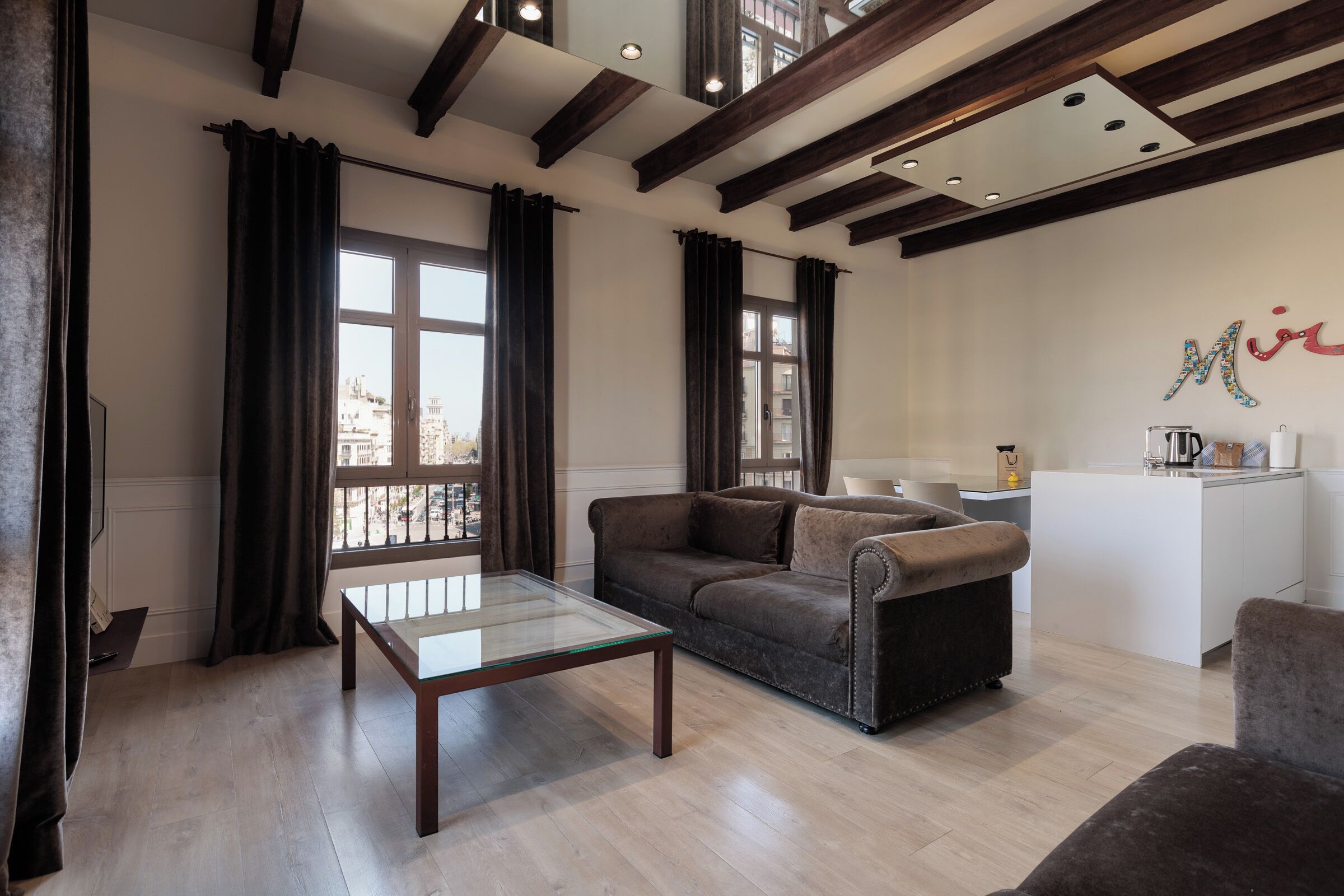 A living room with a sofa, a glass coffee table, and a view of the city through large windows.