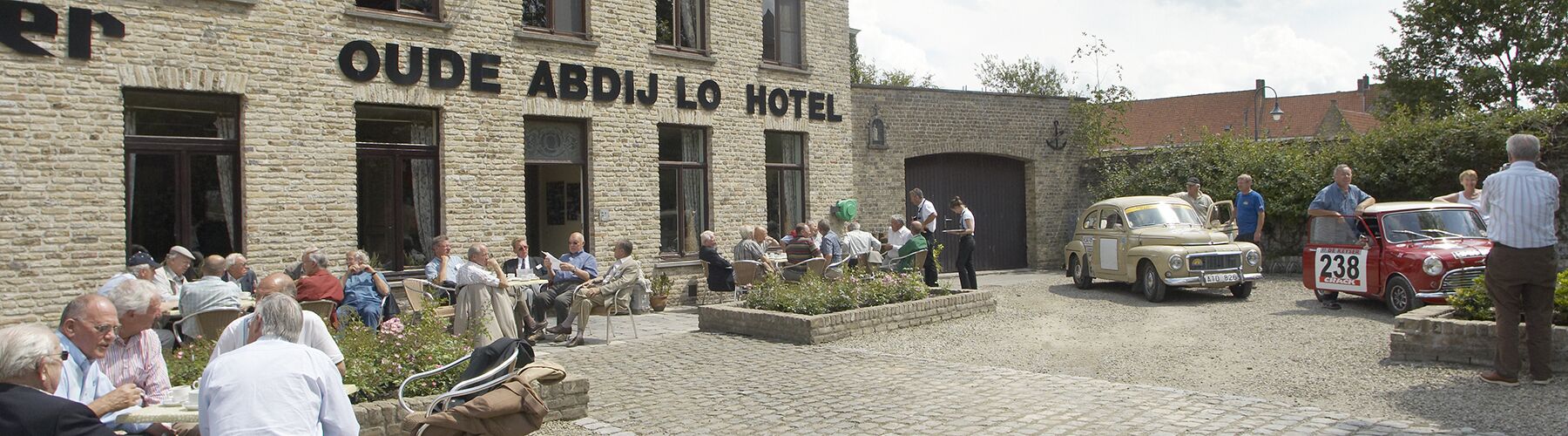 Hotel Oude Abdij Lo con terraza exterior y autos clásicos estacionados en la entrada.