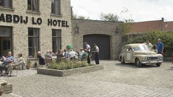 Hotel Oude Abdij Lo con terraza exterior y autos clásicos estacionados en la entrada.