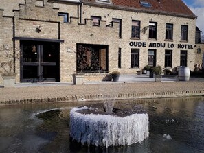 The Oude Aandij Lo Hotel with a stone facade, a large entrance, and a fountain in the foreground. - Hotel Oude Abdij (Lo-Reninge)