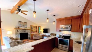 A modern kitchen with a central island, built-in oven, microwave, and refrigerator. There is a seating area with a sofa and a fireplace.