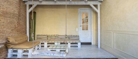 A patio with a swing, a cushioned bench, and a door labeled "COLLIS".