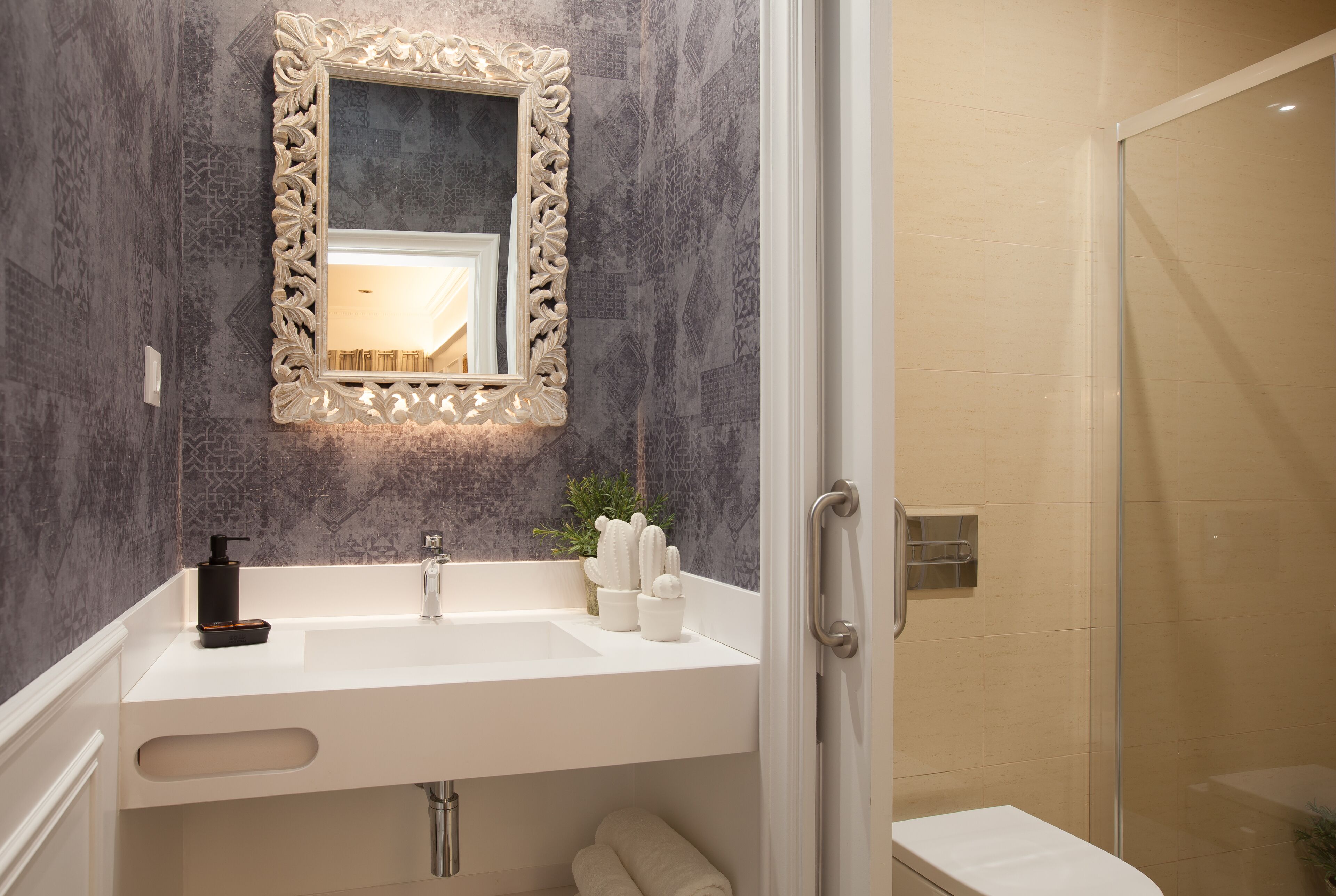 Un baño con lavamanos blanco, espejo con marco decorativo, zona de ducha y perchero.