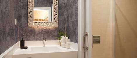Un baño con lavamanos blanco, espejo con marco decorativo, zona de ducha y perchero.