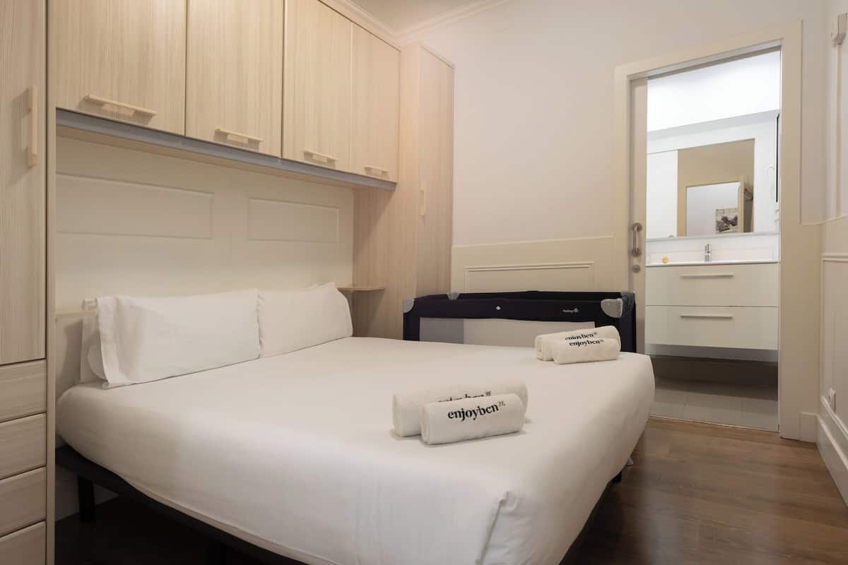 Quarto de hotel com cama, mesa de cabeceira, cômoda e banheiro visível através de uma porta aberta.