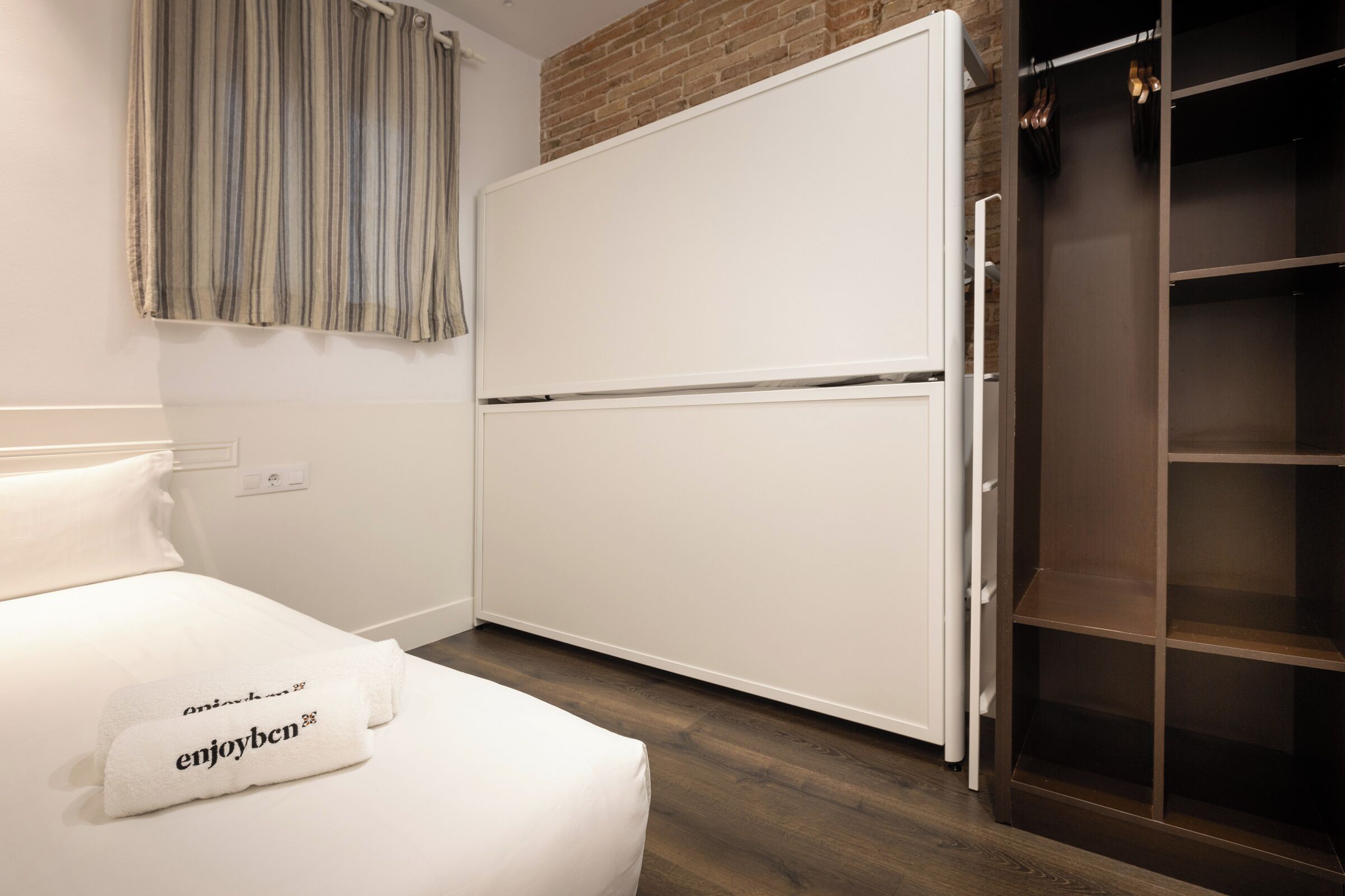 A hotel room with a bed, a white wardrobe, and a wooden floor.