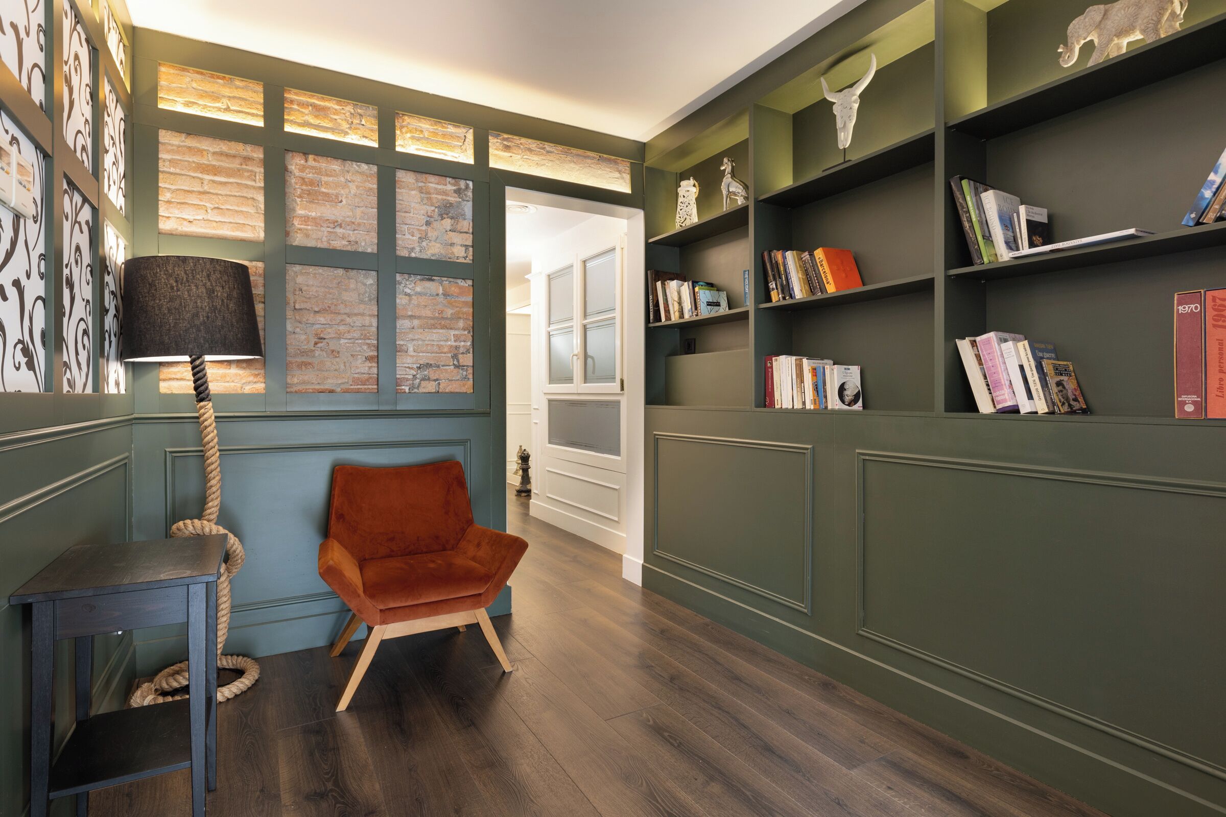 Quarto com piso de madeira, uma cadeira vermelha, um abajur e estantes com objetos decorativos.