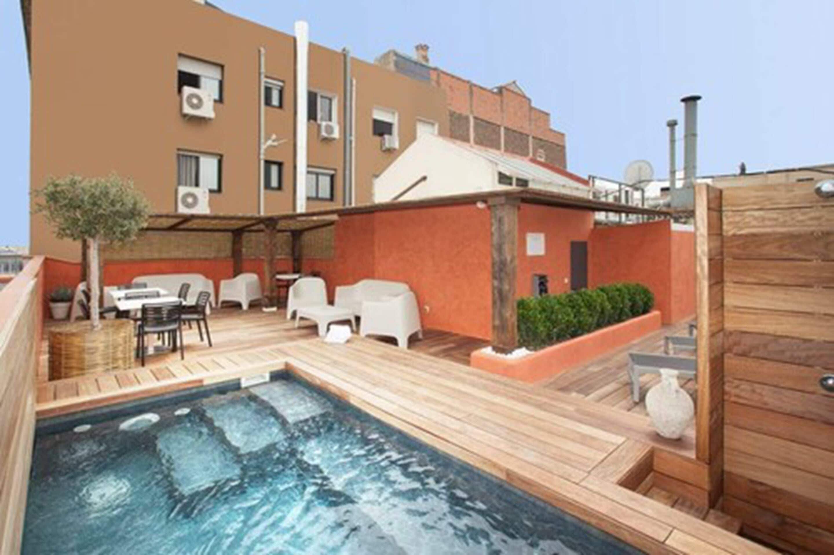 A rooftop pool area with a hot tub, outdoor seating, and a view of the building's exterior.