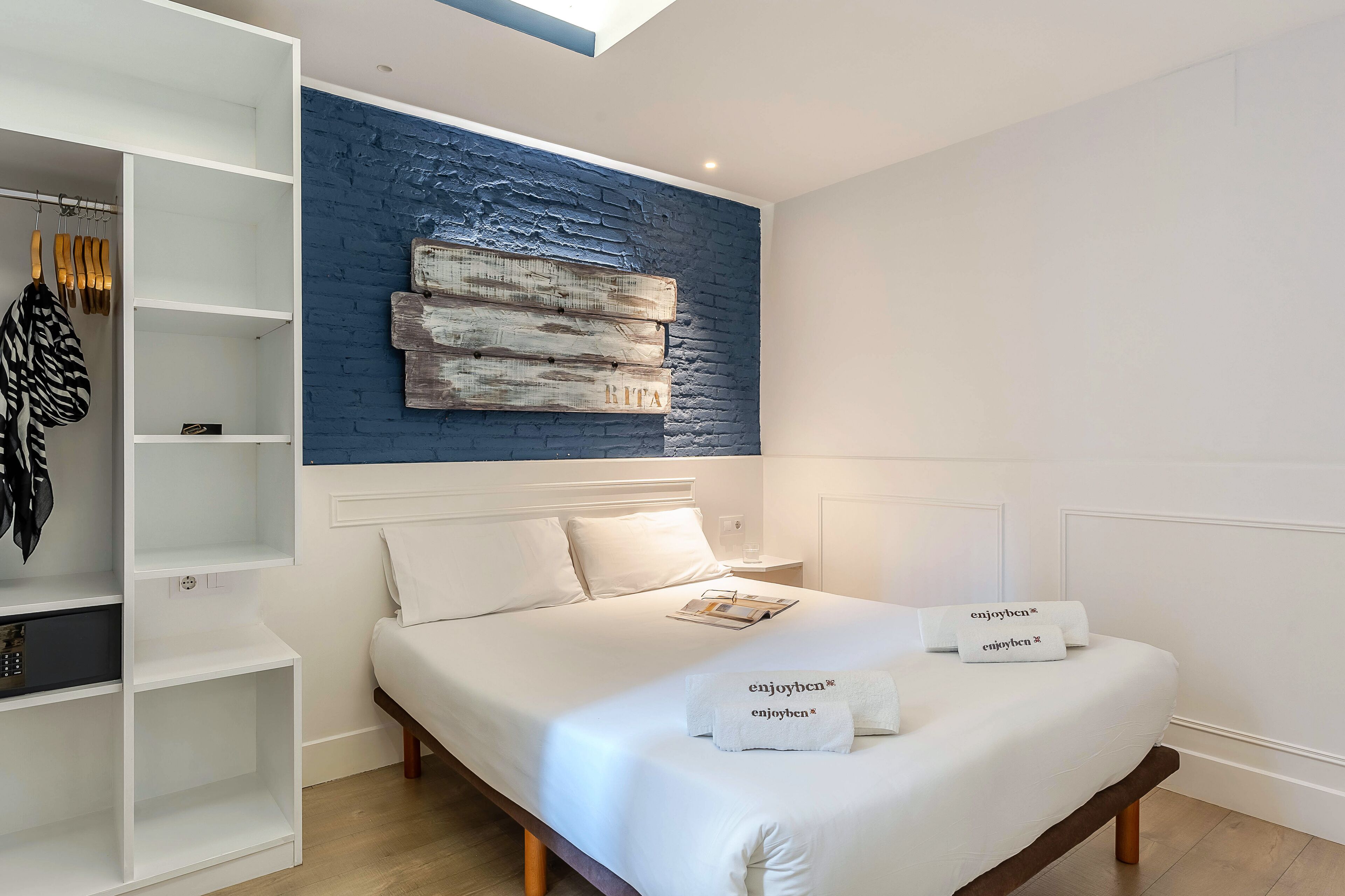 Ein Schlafzimmer mit einem Bett, weißer Bettwäsche, einem Kleiderschrank und einer blauen Wand mit Struktur.