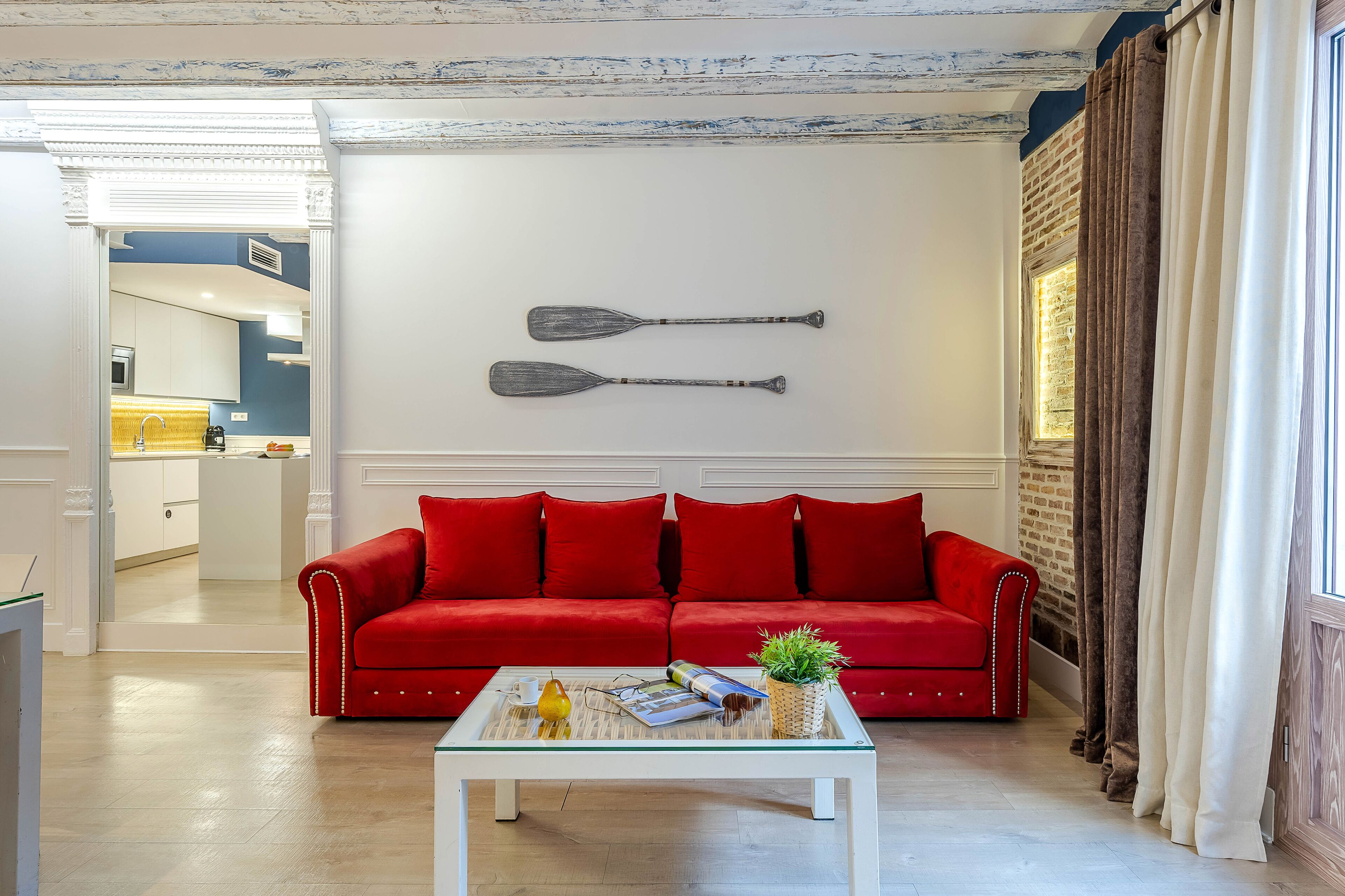Un sofá rojo, una mesa de centro blanca y dos palas en la pared.