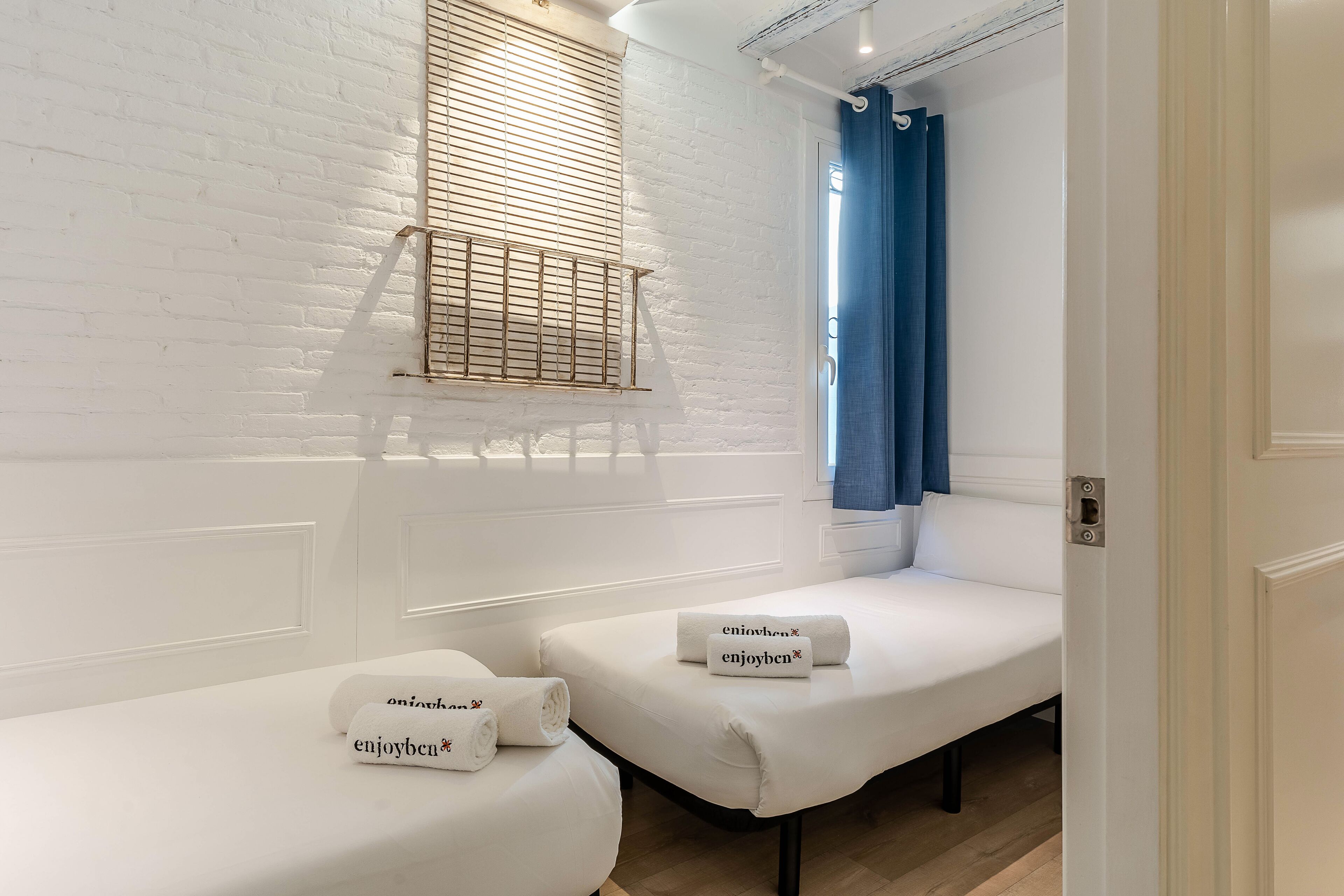 Une chambre avec deux lits blancs, chacun agrémenté d’une serviette sur laquelle est inscrit « enjoyben ».