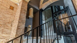 A staircase with a wrought iron railing, brick walls, and a large window with a view of the interior. - Enjoybcn Colon Apartments (Barcelona)