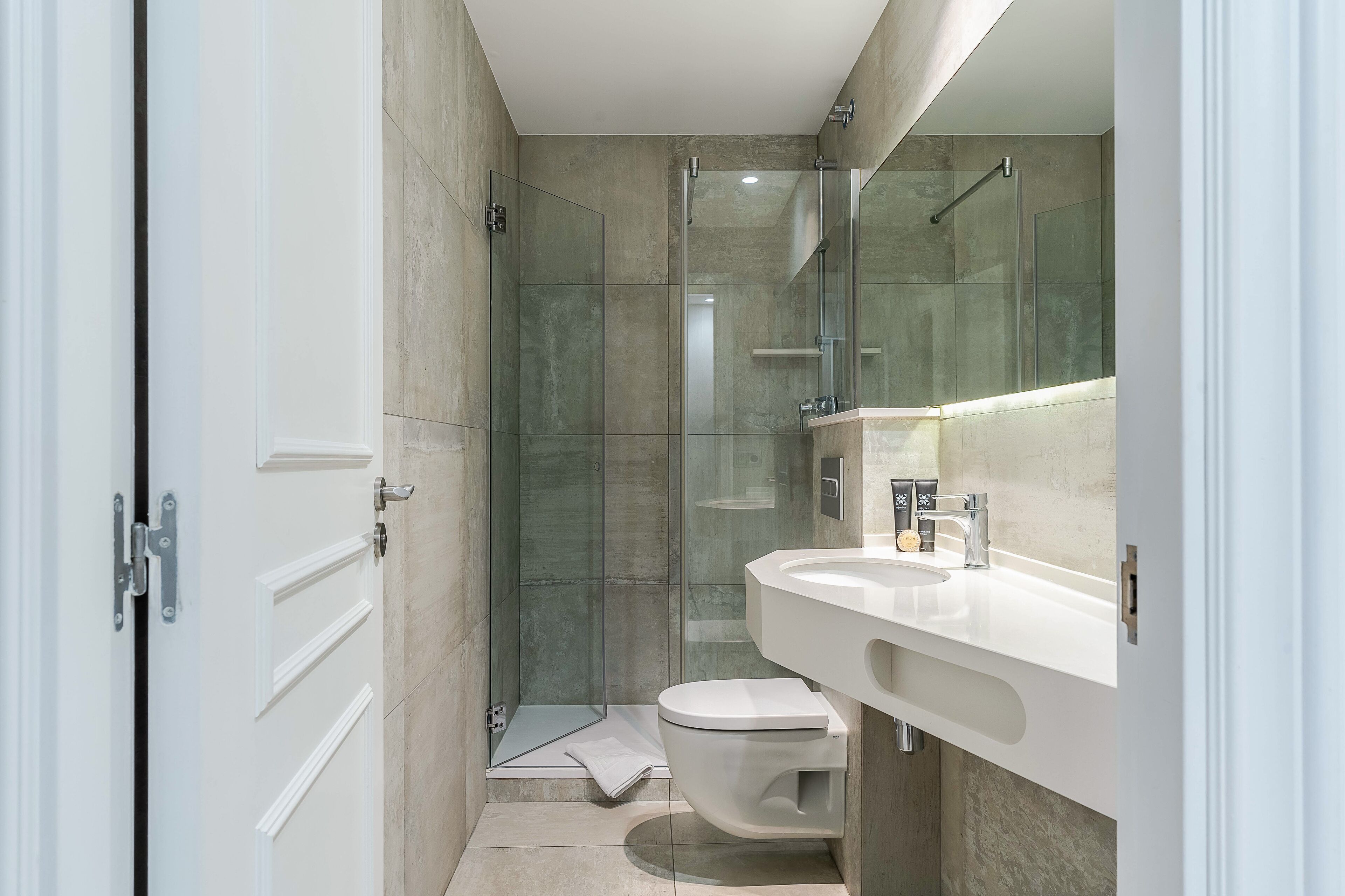 Un baño moderno con cabina de ducha de vidrio, inodoro blanco y un espejo grande sobre el lavamanos.