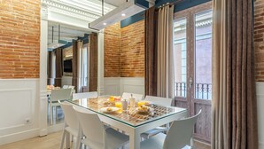 A dining area with a glass table, white chairs, and a brick wall. - Enjoybcn Colon Apartments (Barcelona)