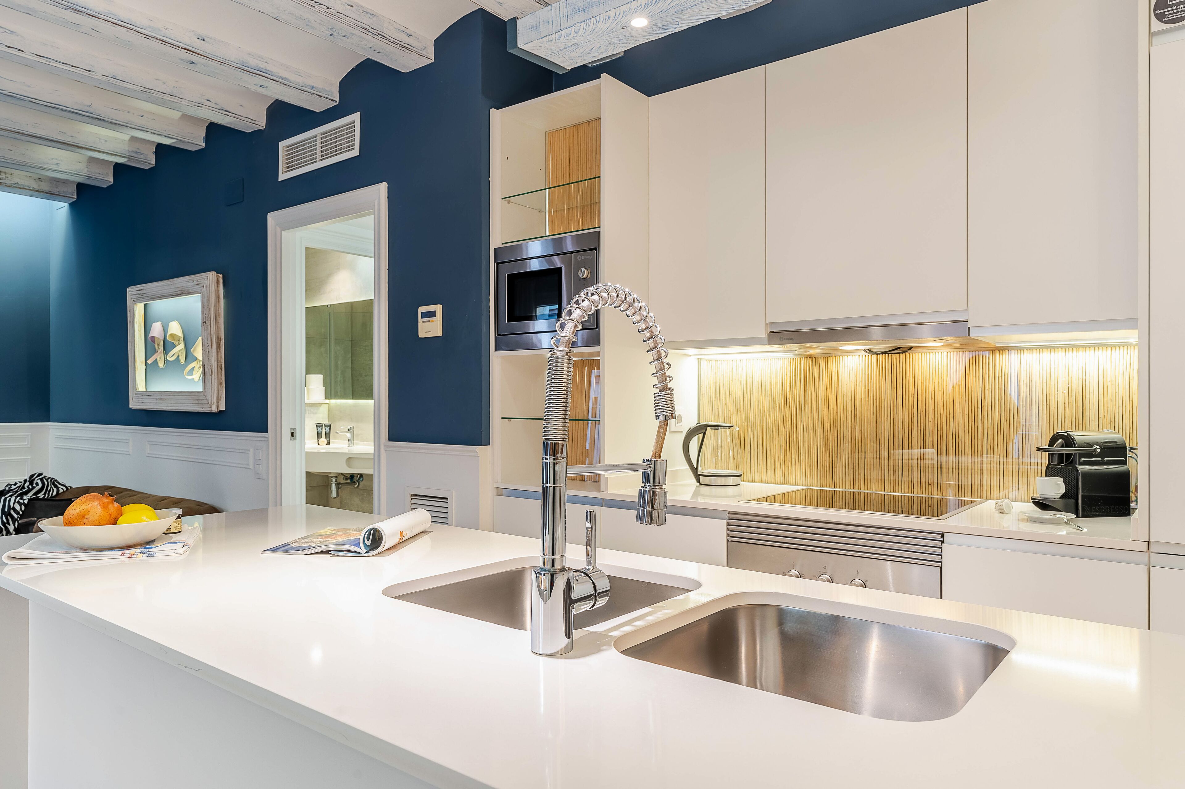 A modern kitchen with white countertops, stainless steel sinks, and a built-in oven.
