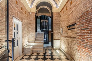 A hallway with brick walls, a checkered floor, and a staircase leading to an upper level. - Enjoybcn Colon Apartments (Barcelona)