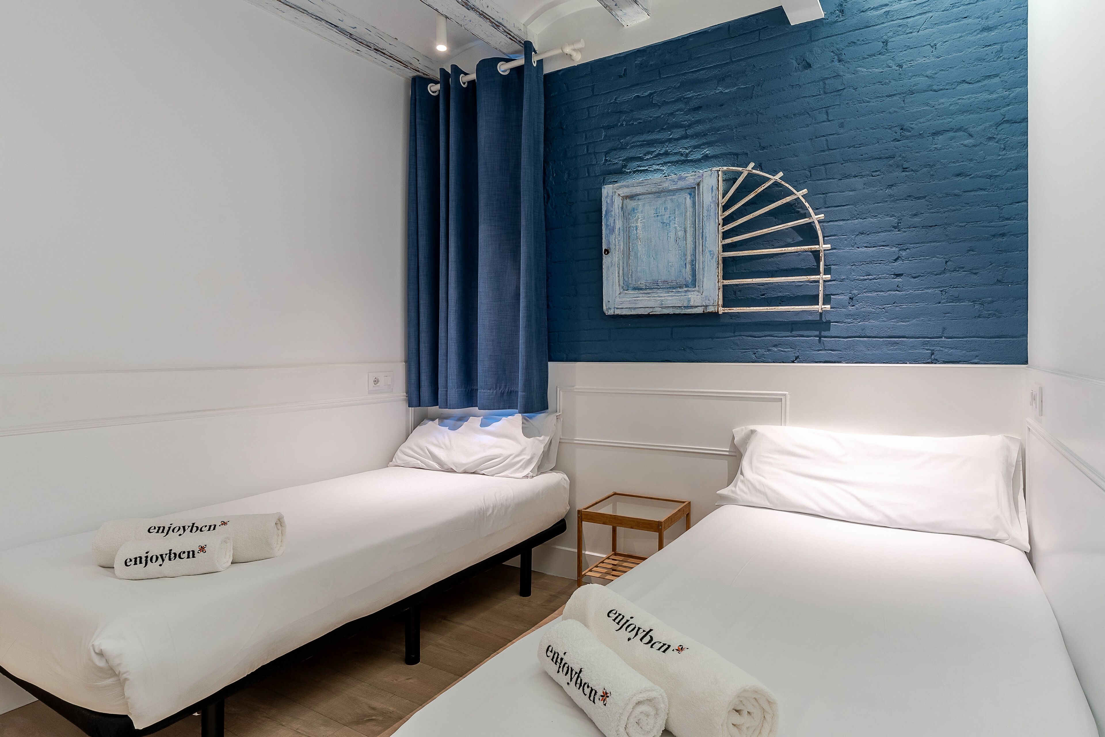 A room with two beds, each with a rolled towel and a pillow.