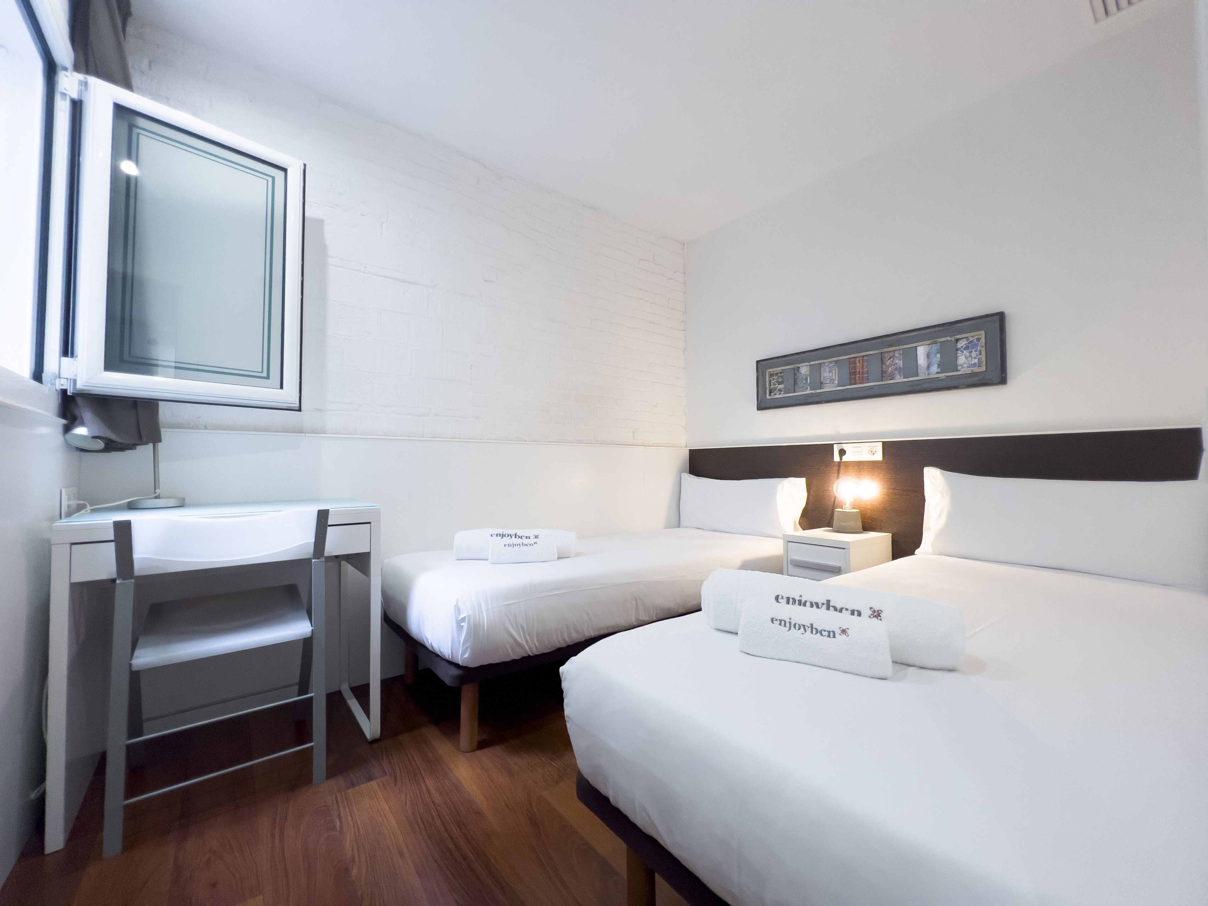 A hotel room with a desk, two beds, a mirror, and a framed picture on the wall.
