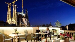 An outdoor patio with tables and chairs, a view of a building with spires, and potted plants. - Enjoybcn Gaudi Apartments (Barcelona)