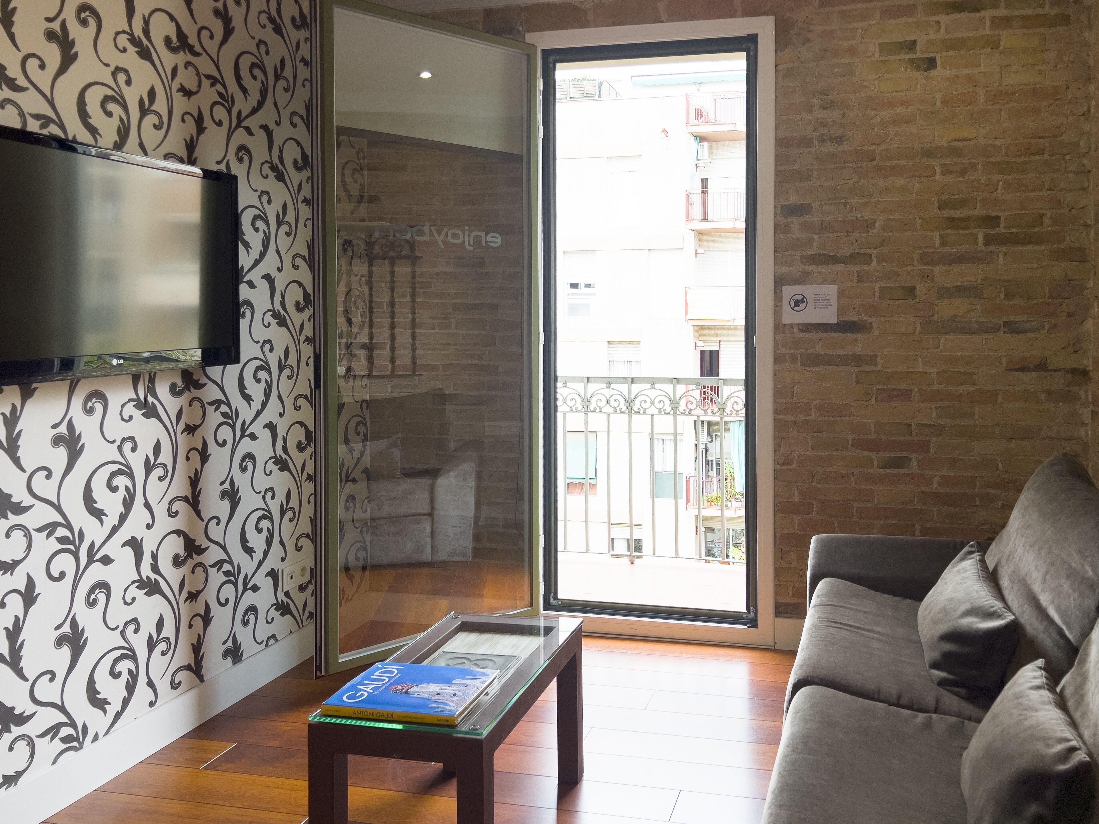 Un salon comprenant un canapé, une table basse avec un livre, un téléviseur fixé au mur et une porte-fenêtre coulissante donnant sur un balcon extérieur.