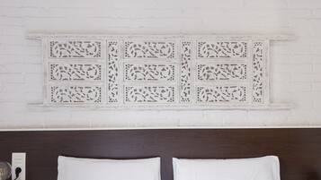 Un dormitorio con pared de ladrillo blanco, un panel decorativo blanco sobre la cama y cabecera de madera oscura.